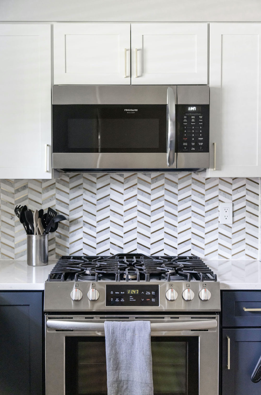 White and blue kitchen cabinets with cooking range and fishbone tile pattern backsplash after renovation
