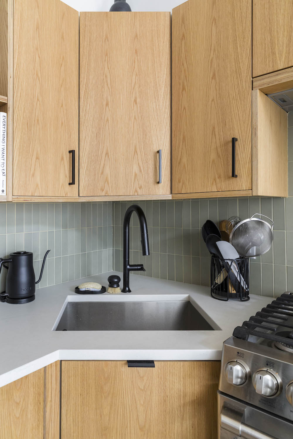 Wood cabinets, sage green tile background, black hardware
