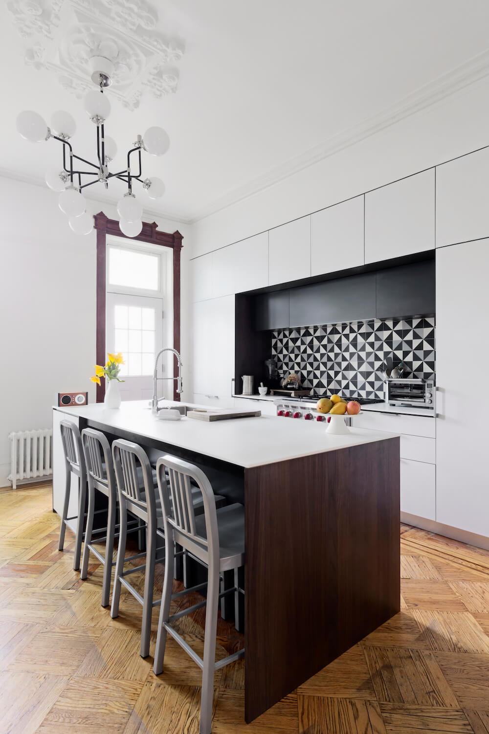 Ceiling lighting under white kitchen island on hardwood floor across white open kitchen after renovation
