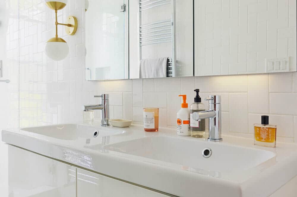 double sink with glossy white vanity and polished brass light fixture after renovation