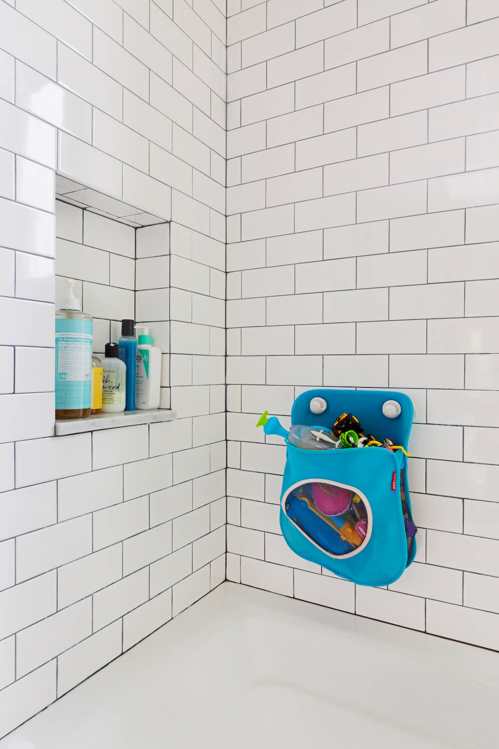 White subway tiles with gray grout and shower niche over white bathtub after renovation