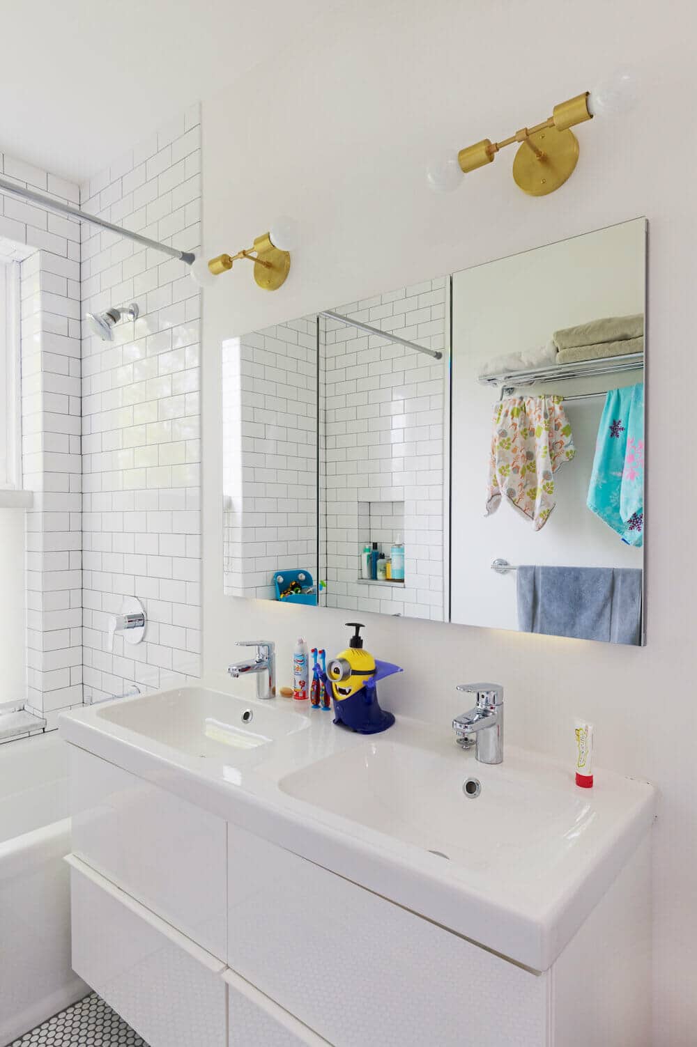 White bathroom with glossy double vanity under double sink and frameless glass shower doors after renovation