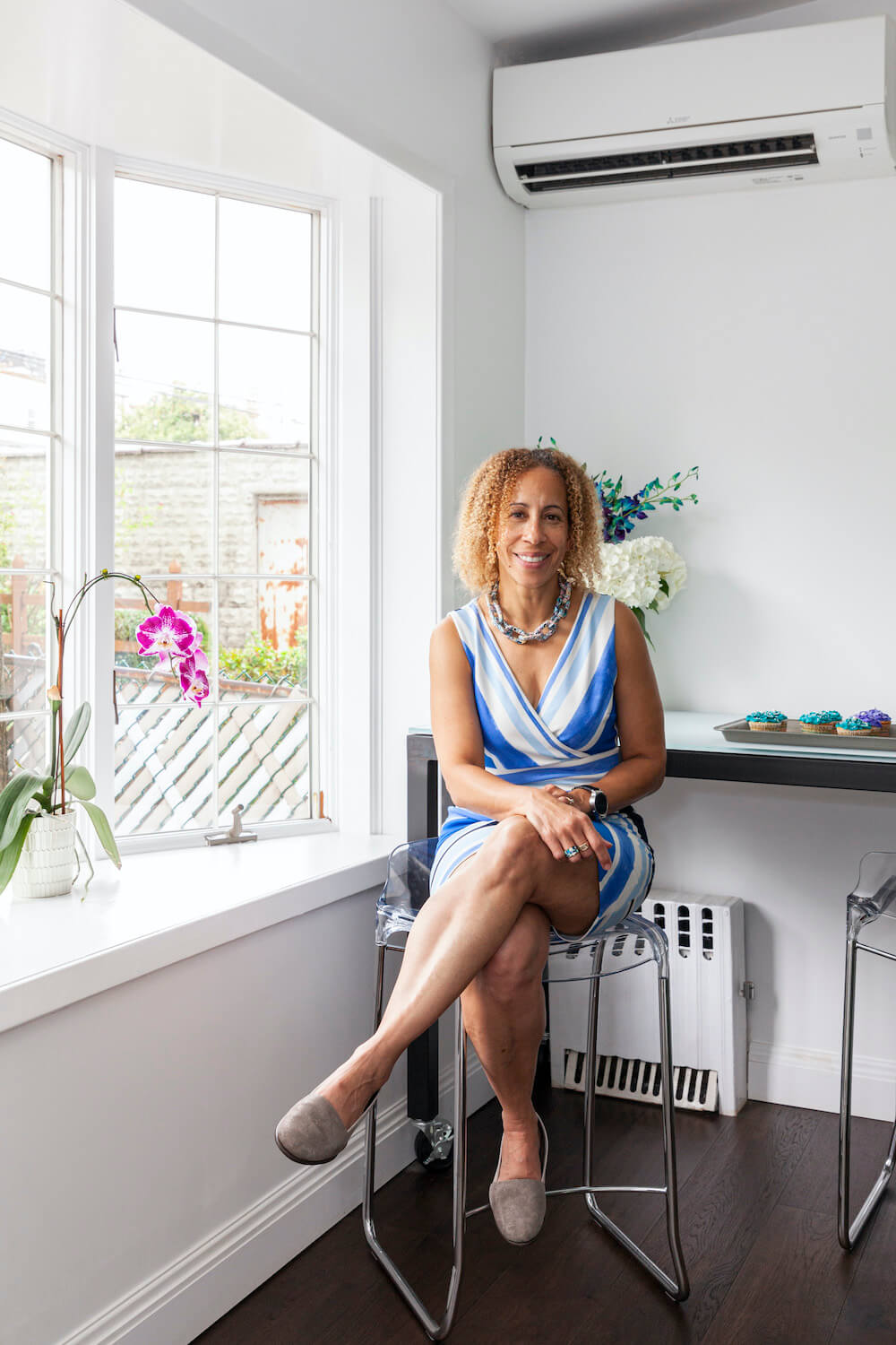 laura sitting on a chair under wall mounted air conditioner and next to a bay window after renovation