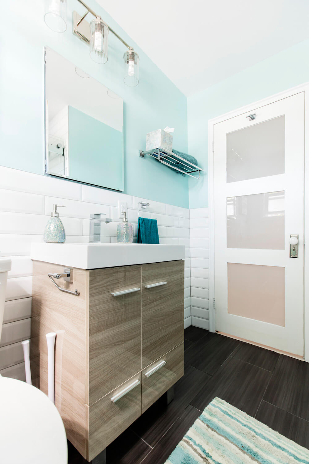 Brown vanity with long cabinet pulls in a white and blue bathroom with dark floor after renovation