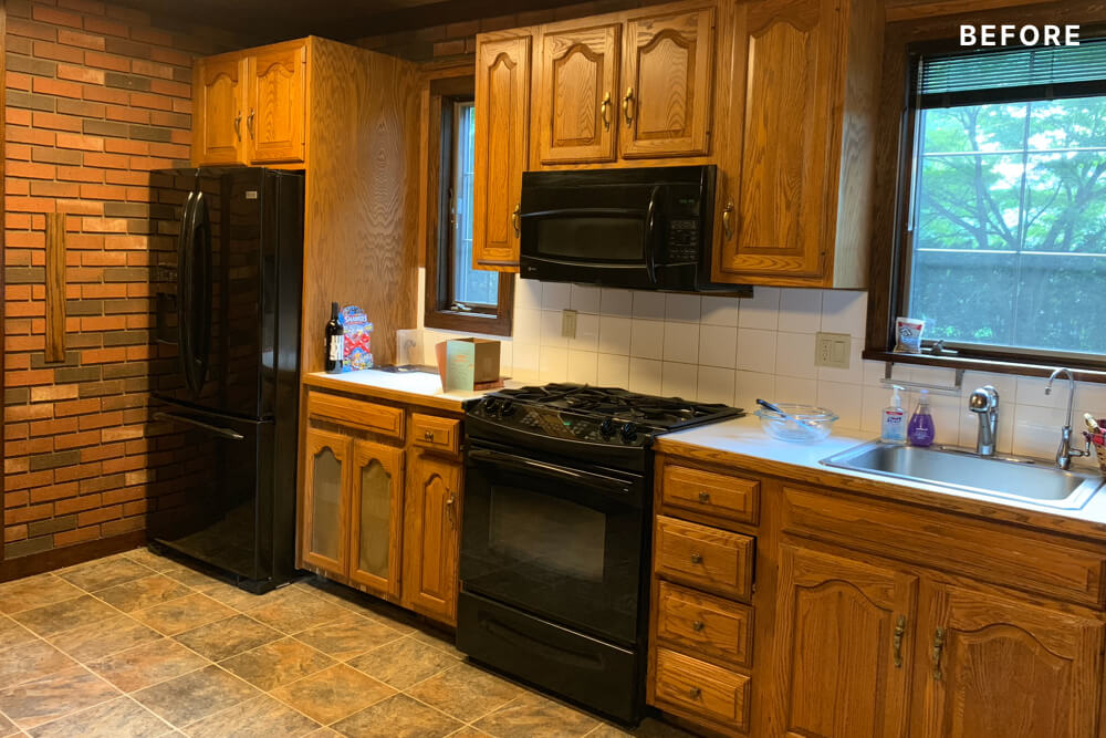 kitchen with windows and black appliances and oak cabinets and brick wall before renovation