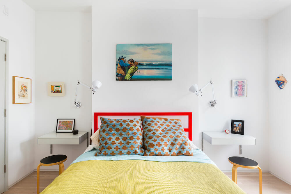 White bedroom with bed and red headboard and paintings on the wall after renovation
