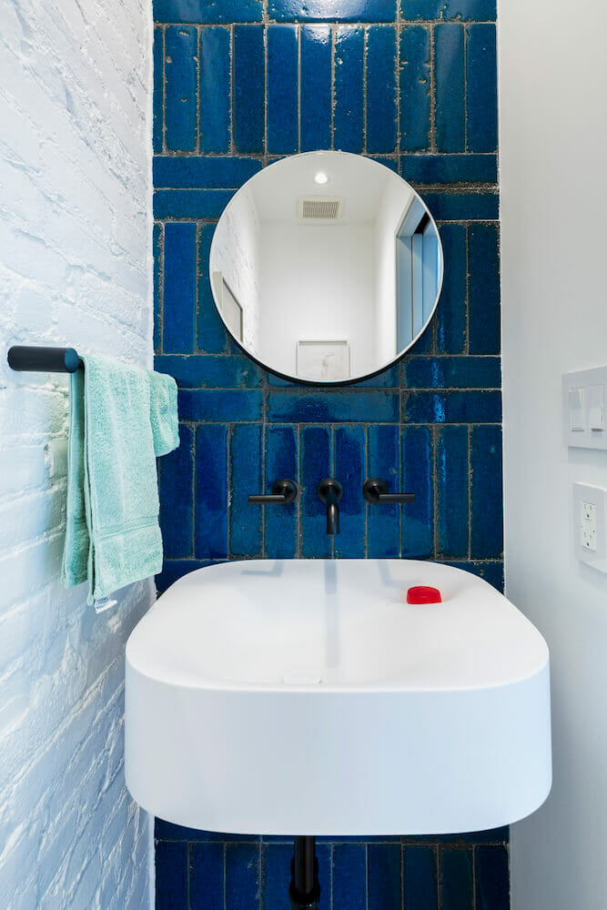 White and blue powder room with circular mirror and white sink after renovation
