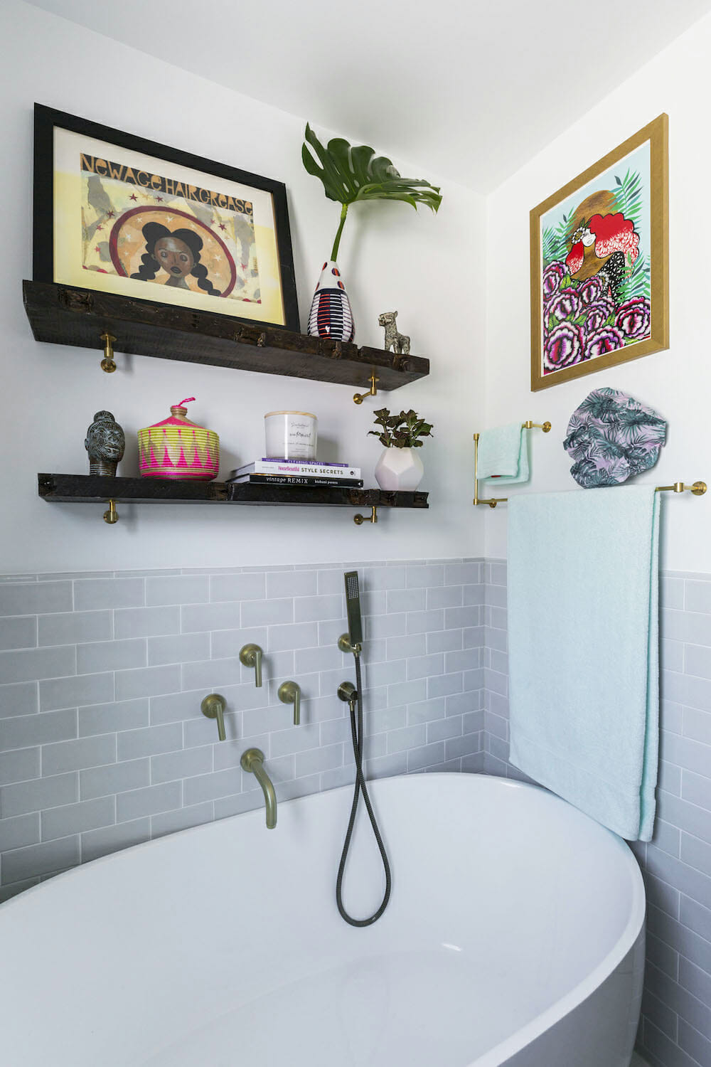 free standing bathtub with gray tiles on half walls and gold towel bars and two floating shelves after renovation