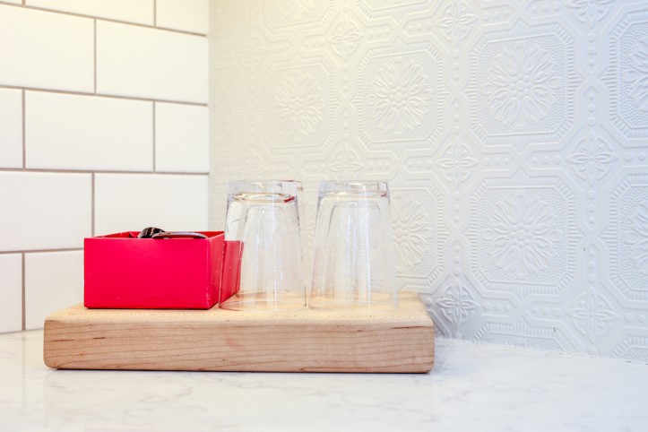 stone countertop with wooden block and glasses along with patterned wallpaper and white subway tiles after renovation