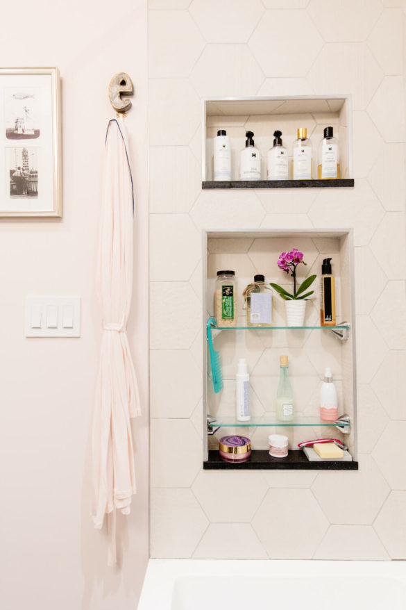 off-white hexagon tiles on walls and white bathtub and recessed shelves on wall after renovation