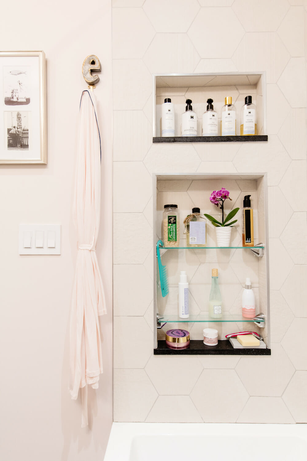 off-white hexagon tiles on walls and white bathtub and recessed shelves on wall after renovation