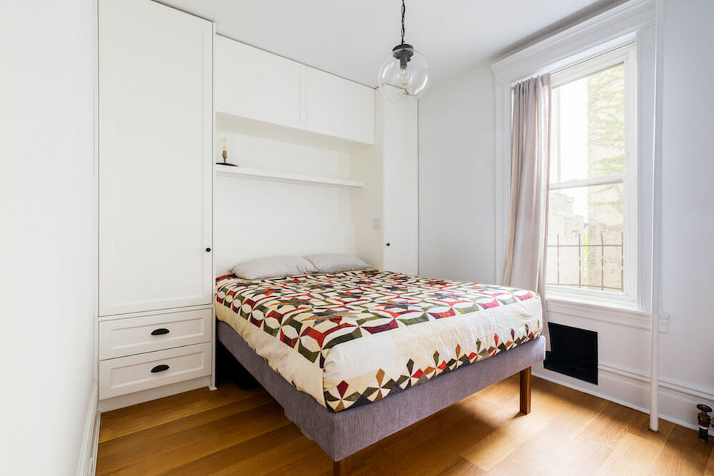 large white cabinets with drawer and a bed near large window after renovation