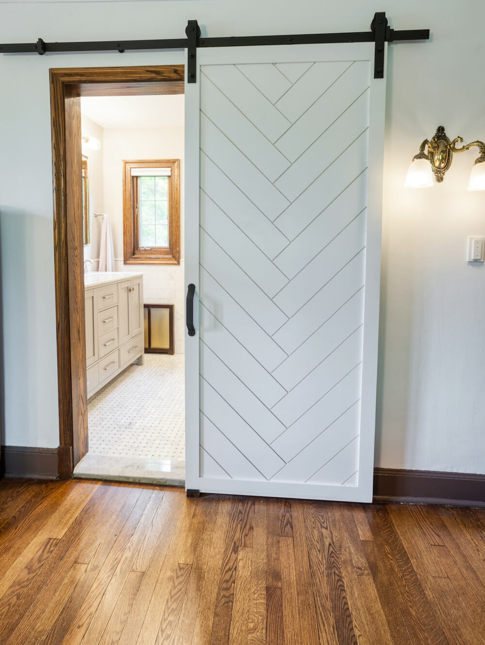 bedroom with hardwood floors and natural wood trims and sliding barn door with chevron design to bathroom after renovation 