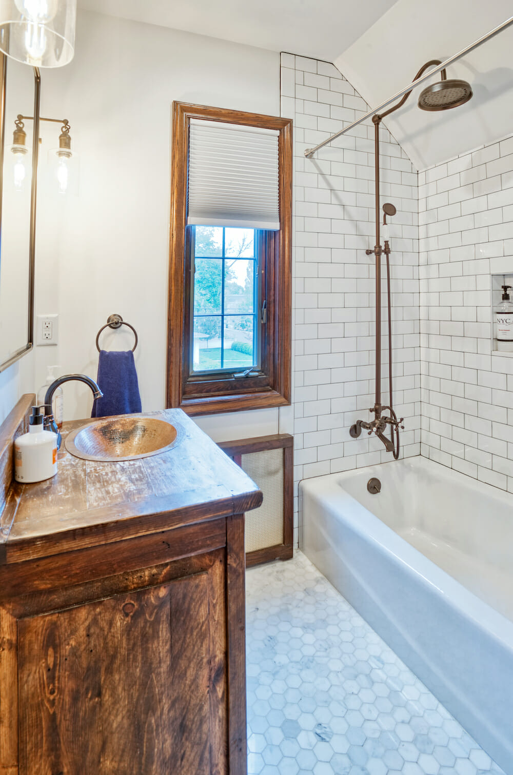 bathroom with rustic vanity with undermount sink and small white floor tiles and bathtub and window with natural wood frames after renovation